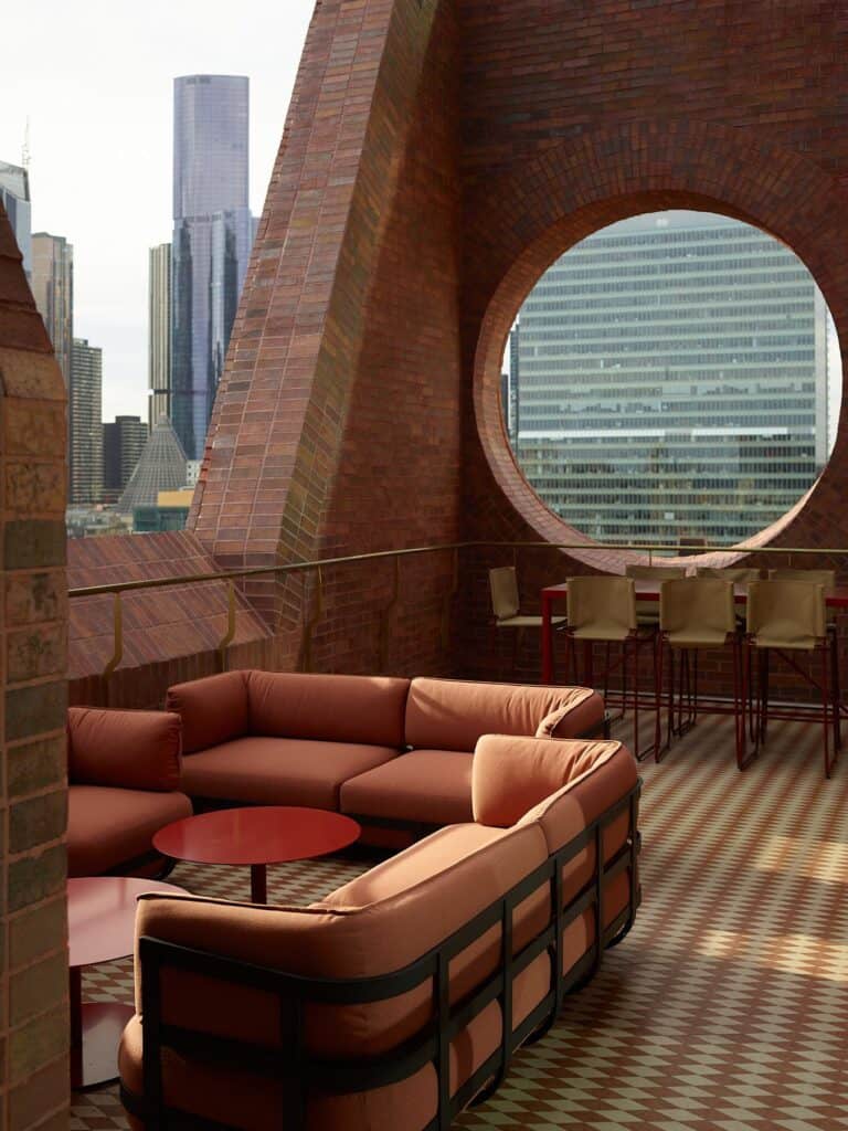 Terracotta sofas and red tables on the checkerboard-tiled Mid Air terrace at Melbourne Place Hotel beneath a giant brick oculus