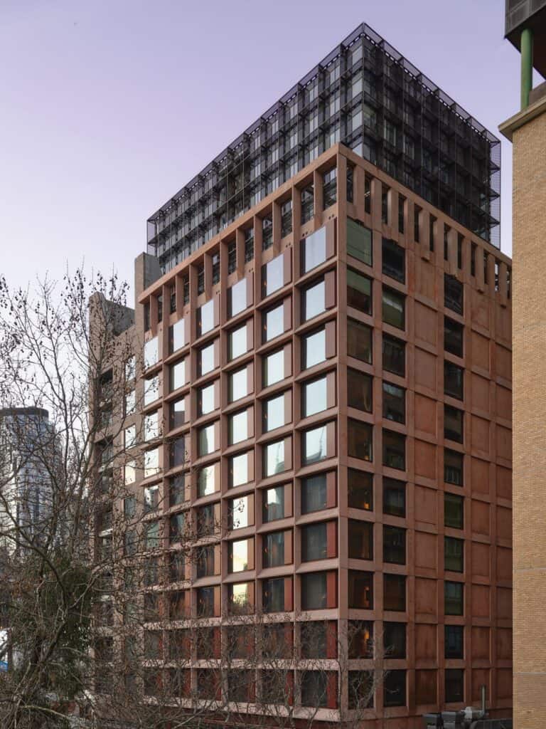 Deeply modelled pink precast concrete grid of guest-room windows at Melbourne Place Hotel, crowned by a dark corten brise-soleil