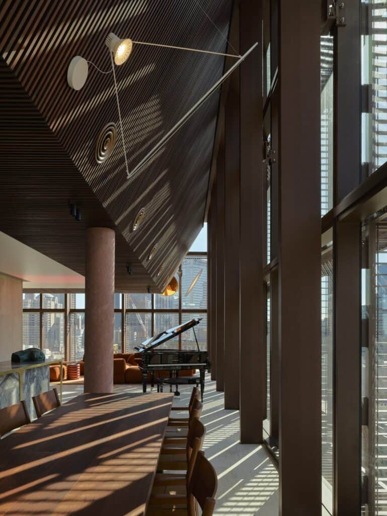 Penthouse at Melbourne Place Hotel with a raked slatted timber ceiling, long jarrah dining table, black grand piano and tall windows in low sun