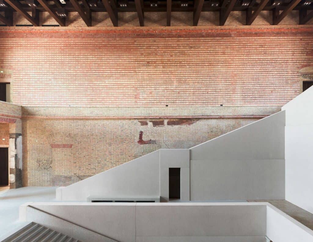 Upper wall of the Neues Museum staircase hall in exposed brick with traces of lost decoration, above the angular white concrete flights of the new staircase
