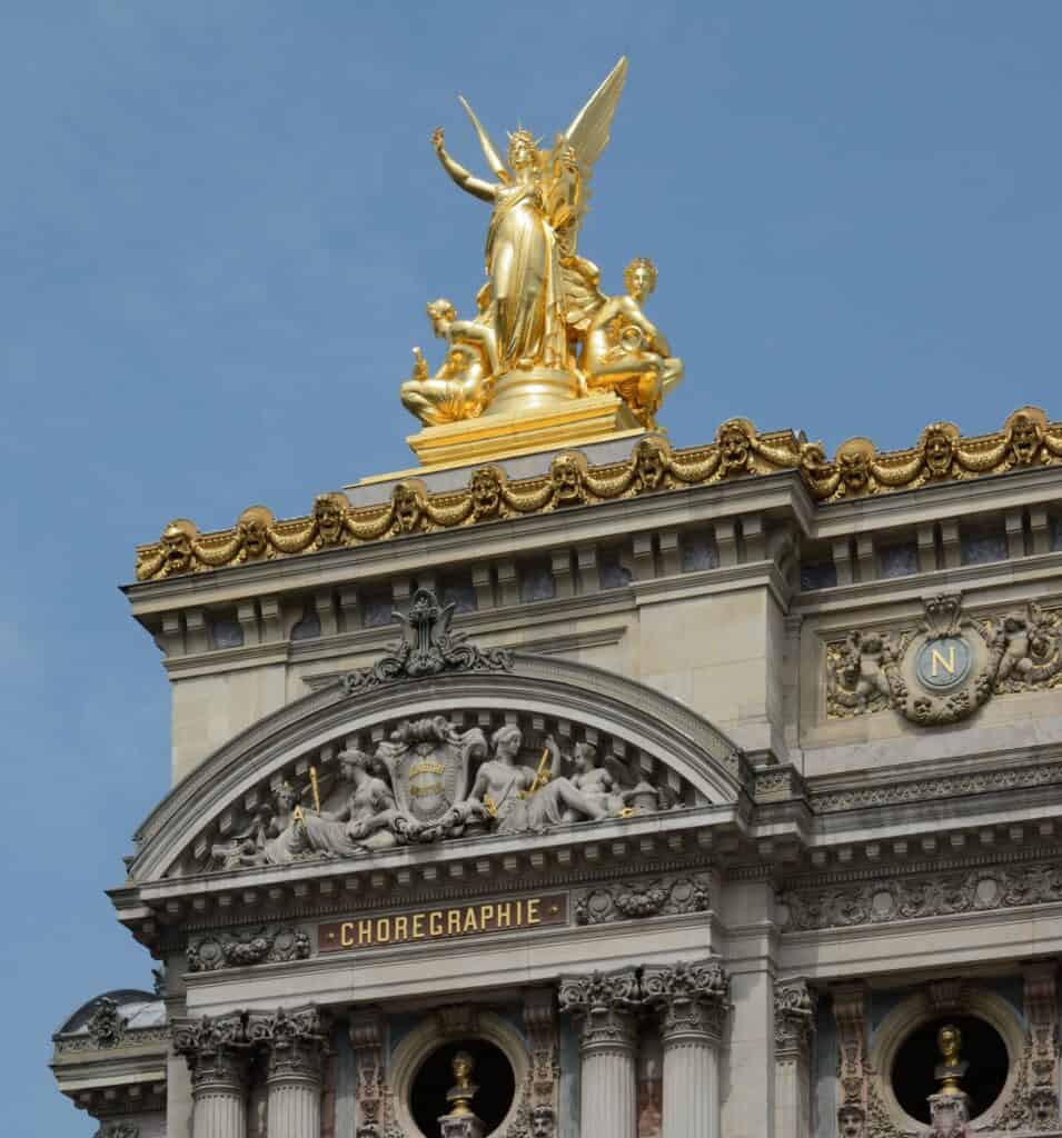 Gilded statue group of Harmony by Charles Gumery crowning a corner pavilion of the Palais Garnier, above a carved pediment and the inscription Chorégraphie against a clear blue sky