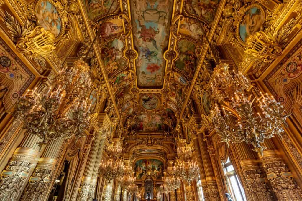 Grand Foyer of the Palais Garnier looking up past crystal chandeliers and gilded columns to a long painted and coffered ceiling