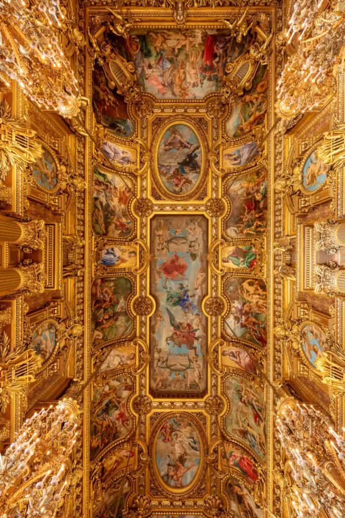 Length of the Grand Foyer ceiling at the Palais Garnier, a row of painted panels framed in deep gilded relief running between glittering chandeliers