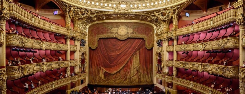 Panoramic view of the Palais Garnier auditorium, gilded tiers of red boxes framing the stage and its painted red and gold curtain
