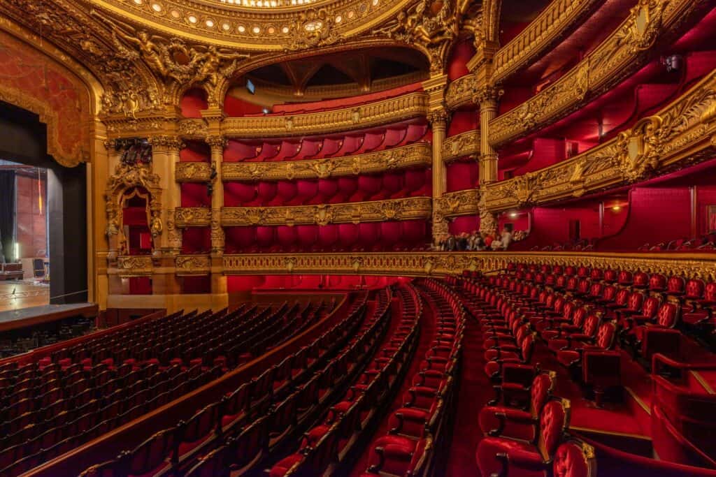 Red velvet seats of the stalls in the Palais Garnier auditorium rising towards the curved tiers of gilded boxes and the stage opening