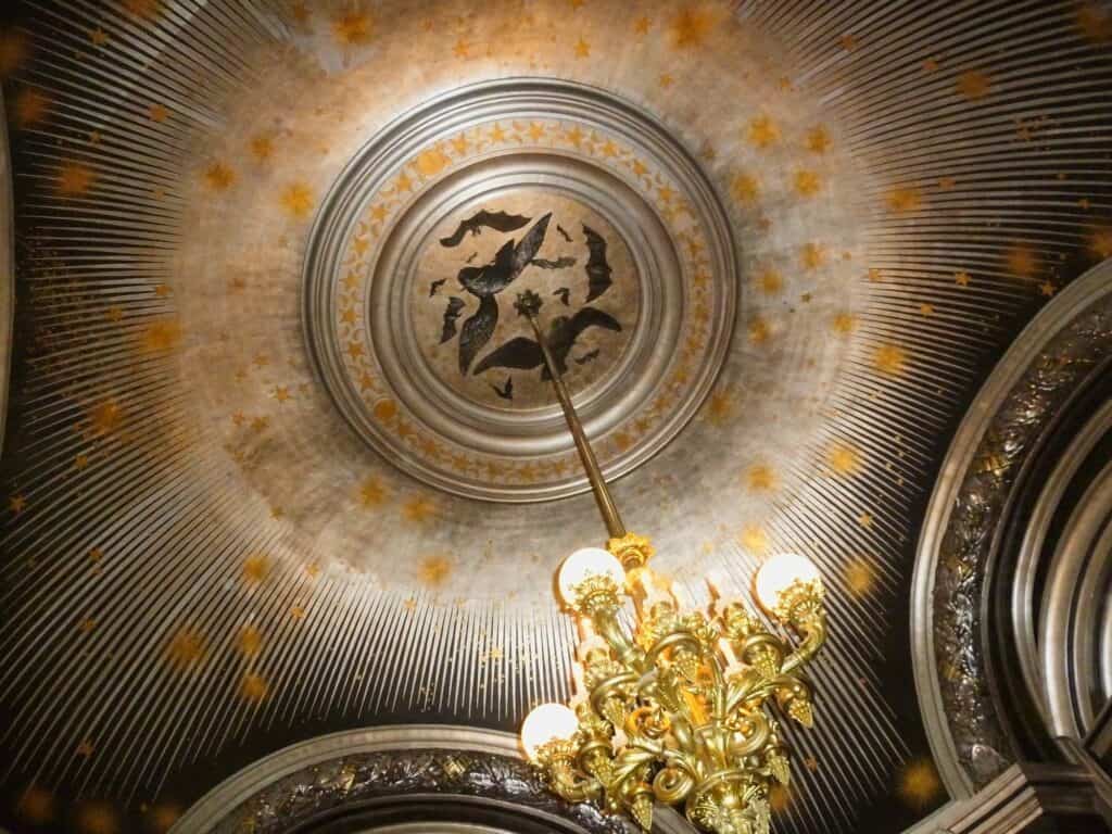 Silvered ceiling of the Salon de la Lune at the Palais Garnier, rays of silver and gold stars spreading from a central medallion of bats and an owl above a gilded chandelier
