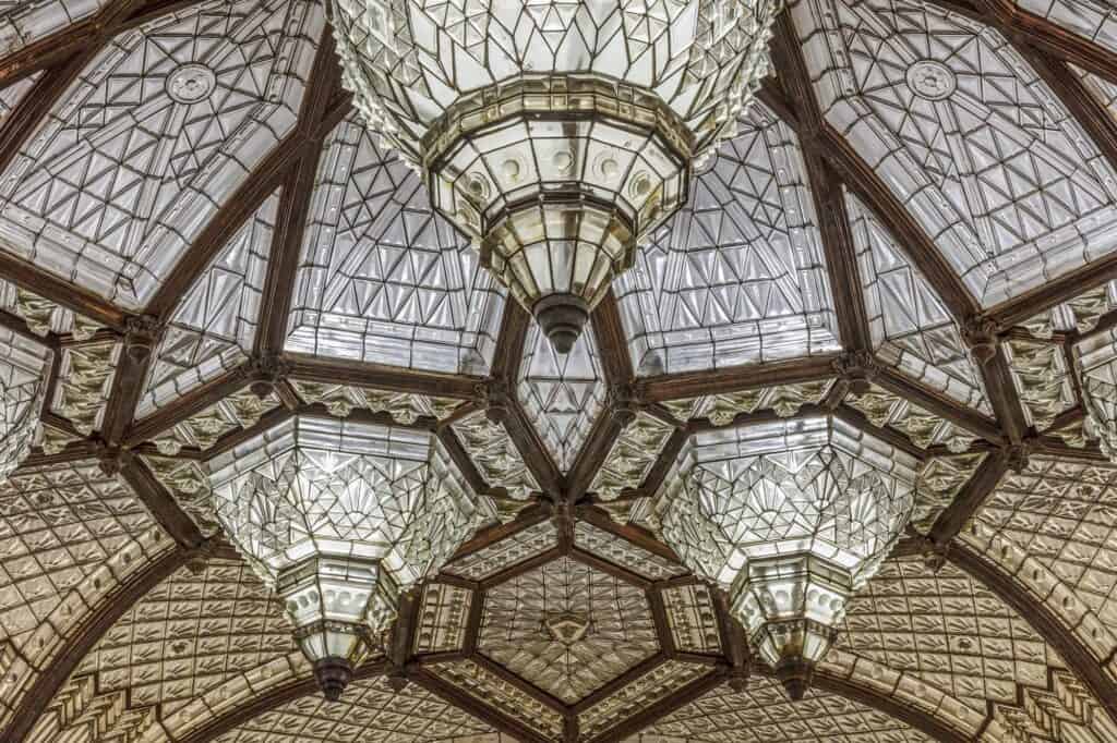 Looking up into a glass dome of the Paris Court arcade, a star-shaped pattern of dark ribs and pale leaded glass radiating around clustered crystal chandeliers