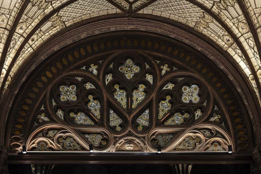 Great semicircular stained glass window in the Paris Court arcade, Neo-Gothic tracery of rosettes and trefoils framed by a deep carved timber arch beneath the glazed vault