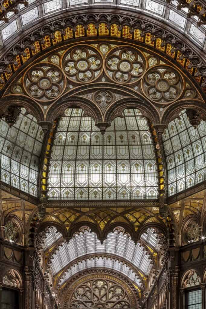 Vertical view of a Paris Court dome, ribbed panels of milky glass between bands of gilded ornament, with a filigreed Moorish arch and a further glass vault below