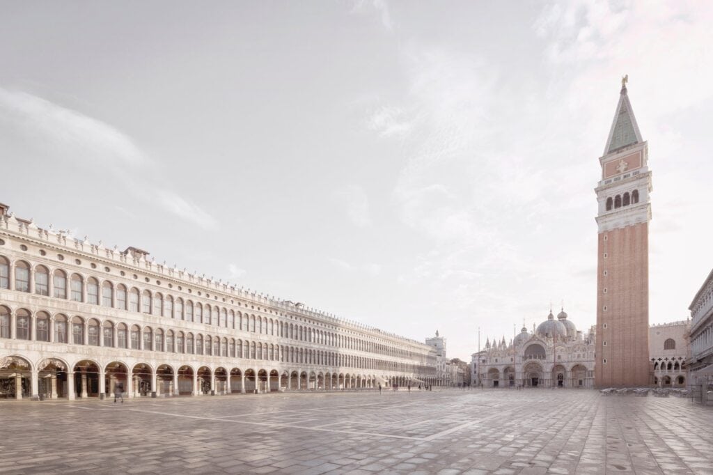 Procuratie Vecchie stretching along the north side of St Mark's Square in Venice, its long arcade and rows of arched windows leading towards St Mark's Basilica and the brick campanile across the almost empty paved square