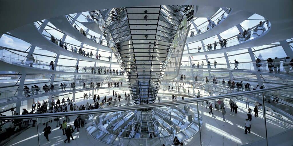 Interior of the Reichstag cupola with the mirrored cone tapering down through the centre and two spiral ramps of visitors winding up the glazed dome in bright daylight