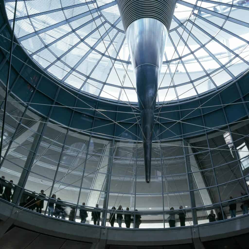 Looking up from the glazed drum of the Reichstag cupola at the slender mirrored cone pointing down from the centre of the steel and glass dome, visitors along the rail below