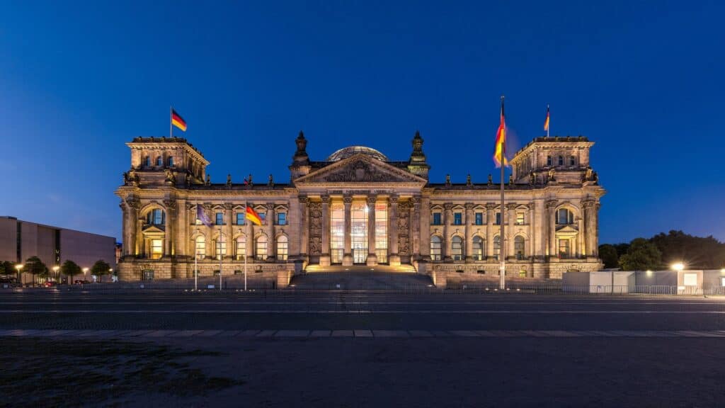 West facade of the Reichstag at blue hour, the portico, corner towers and cupola lit warm gold against a deep blue sky above the empty forecourt