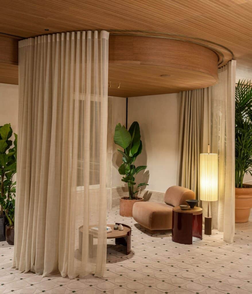 Circular enclosure of sheer curtains hanging from a curved timber ceiling in the spa at Six Senses Rome, with a terracotta armchair, a paper floor lamp and a low wooden table beyond