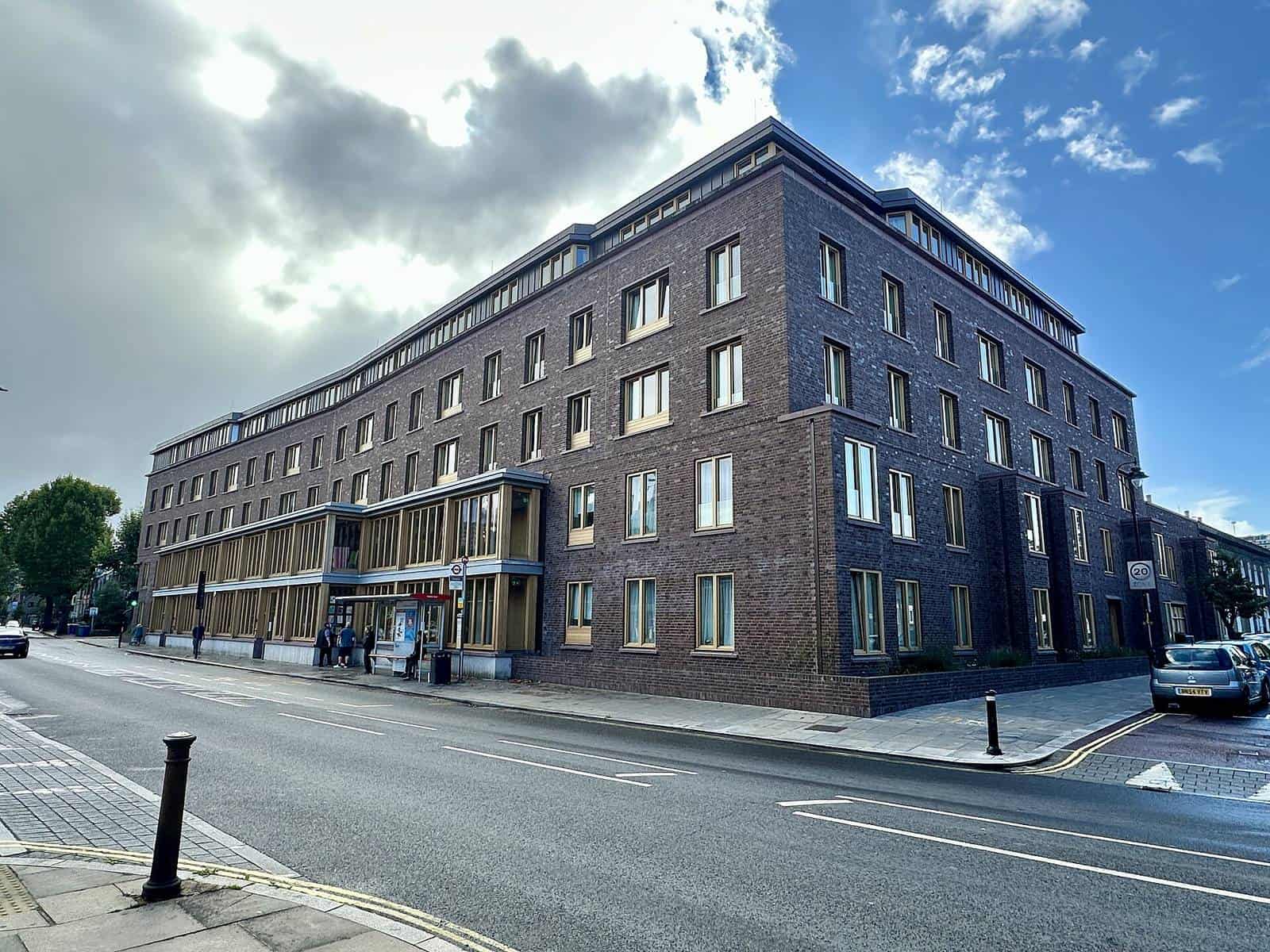 Appleby Blue Almshouse in Bermondsey, London, a long four-storey building in dark brick with rows of large windows, seen along a sunny street