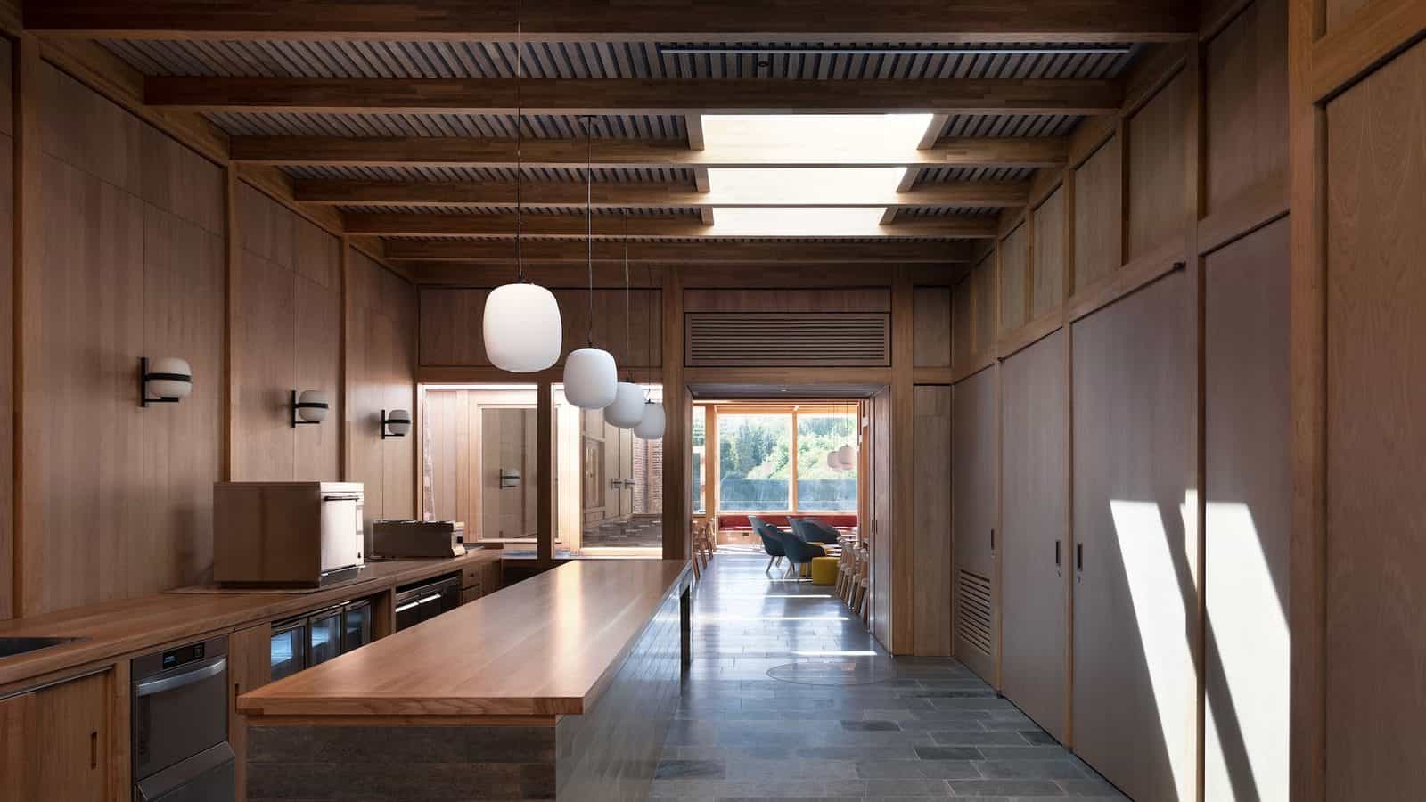 The cafe in the River Wing at Clare College, Cambridge, a long room with an oak-lined ceiling and walls, timber benches, pendant lights and a window at the far end