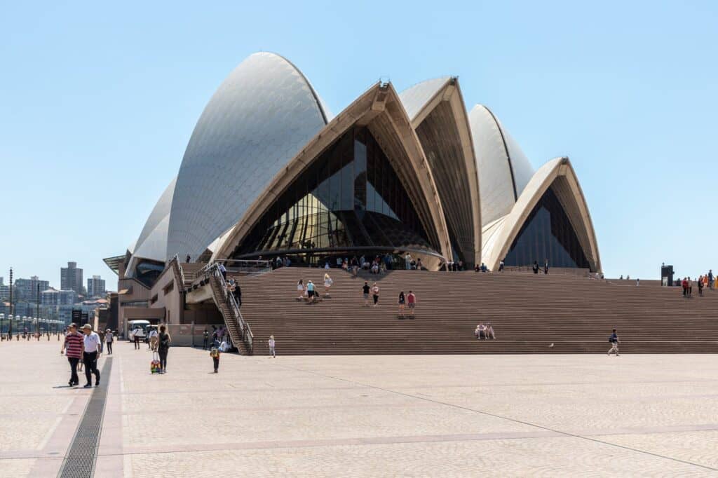 Monumental Steps rising across the forecourt to the Sydney Opera House, visitors climbing towards the soaring tiled shells and glazed foyers under a blue sky