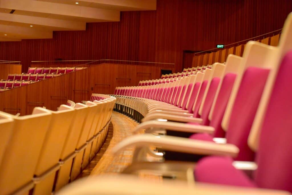 Curving rows of white birch Concert Hall seats with magenta upholstery at the Sydney Opera House, rising towards brush box timber walls and the upper boxes