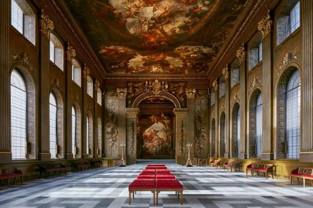 The Painted Hall at the Old Royal Naval College seen from the Lower Hall towards the Upper Hall, Thornhill's restored Baroque ceiling above tall arched windows and red upholstered benches on the patterned marble floor