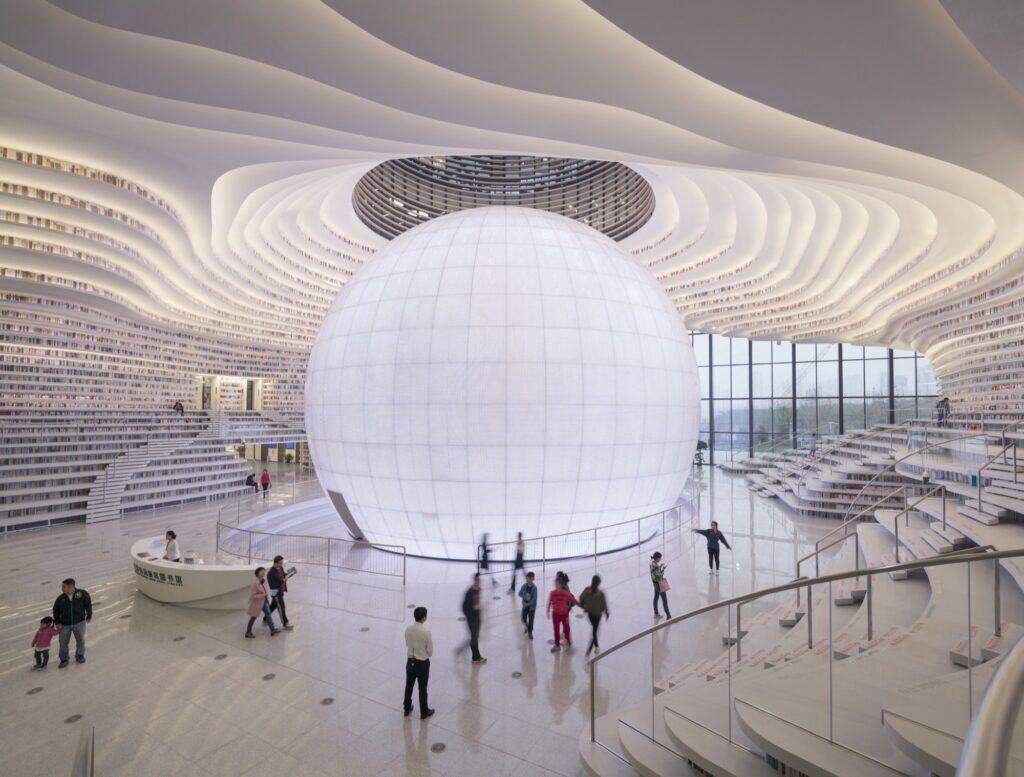 Luminous white sphere of the Eye auditorium inside Tianjin Binhai Library, ringed by terraced bookshelves and visitors