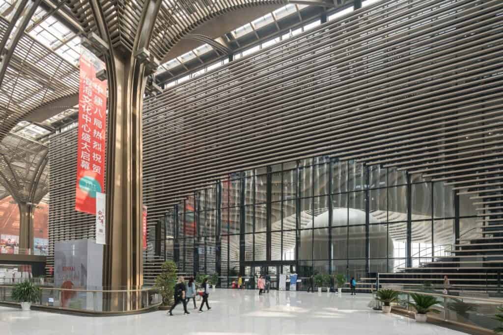 Covered gallery with tree-like columns outside the glazed entrance of Tianjin Binhai Library, the sphere visible inside