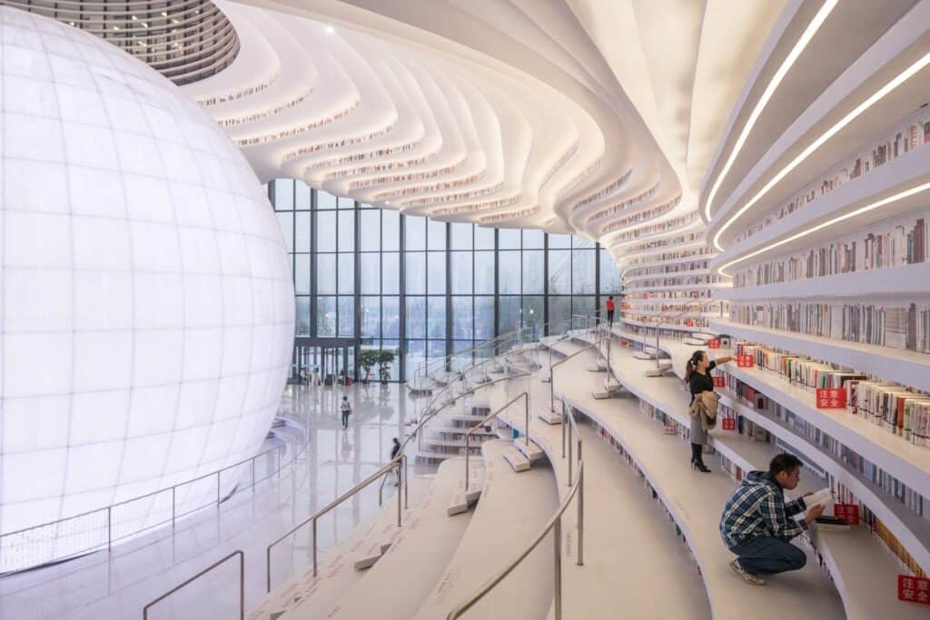 Readers browsing curved terraced shelves beside the luminous sphere at Tianjin Binhai Library