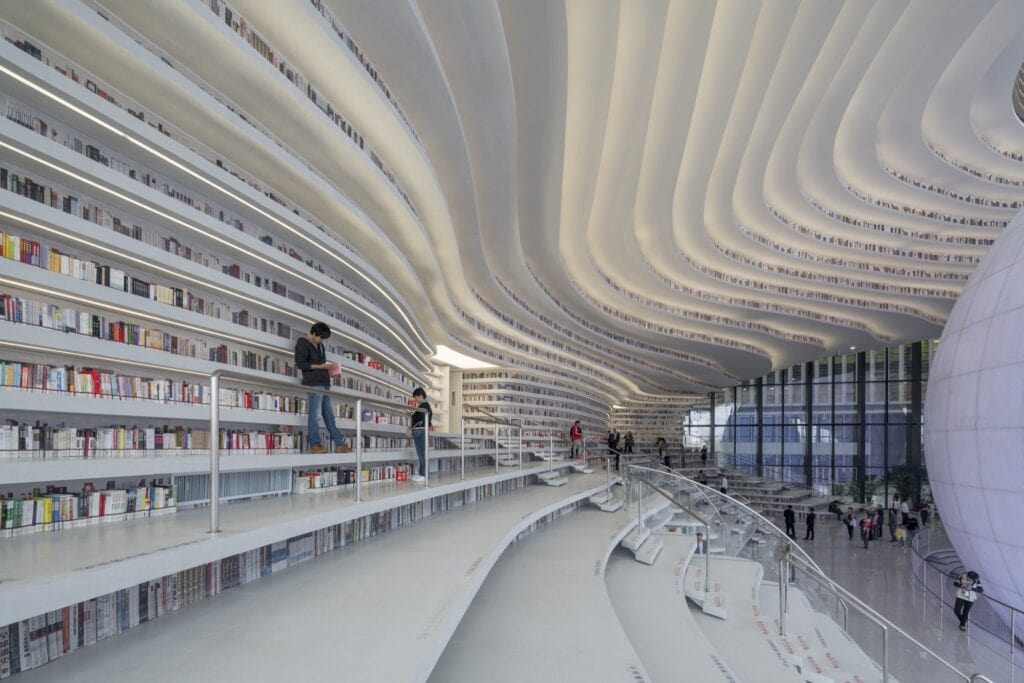 Wave-like white ceiling contours above stepped bookshelves that double as seating and stairs, Tianjin Binhai Library