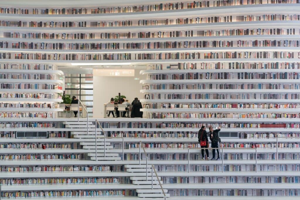 Reading room opening set into a wall of stepped bookshelves at Tianjin Binhai Library, two visitors taking a selfie