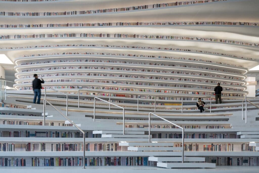Visitors sitting and standing on white bookshelf steps with steel handrails at Tianjin Binhai Library