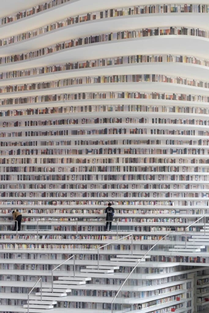 Floor-to-ceiling wall of curving bookshelves with two readers on the terraces at Tianjin Binhai Library