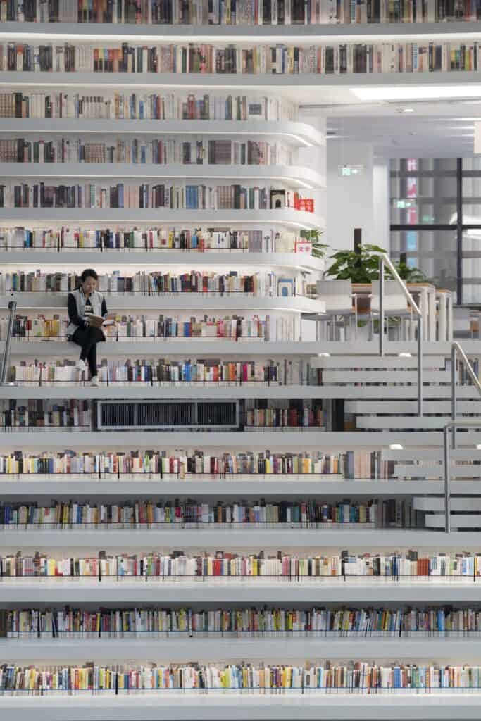 Reader sitting on a bookshelf step among colourful book spines at Tianjin Binhai Library