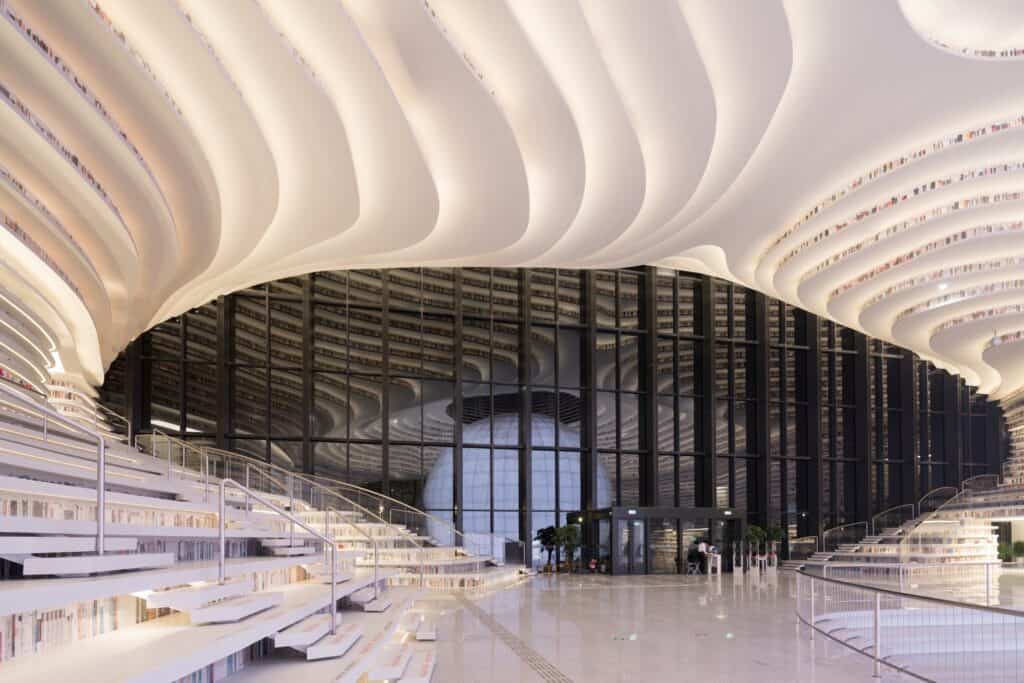 Undulating ceiling contours meeting the dark glazed facade of Tianjin Binhai Library, the sphere reflected in the glass